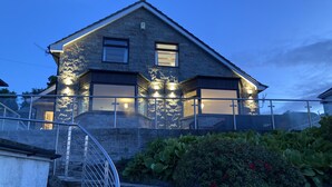 A two-story house with a stone facade, a balcony with glass railings, and a staircase leading to the entrance. - Waters Edge (Stranraer)
