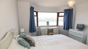 A bedroom with a large bed, a desk, and a view of the sea. - Waters Edge (Stranraer)