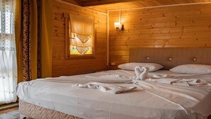 A wooden cabin bedroom with a bed, two bedside lamps, and a window with curtains.