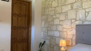 Une chambre avec un mur en pierre, une porte en bois, un lit avec des serviettes pliées, une lampe de chevet et une petite plante en pot.
