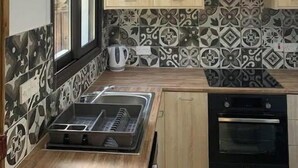 Une cuisine avec des carreaux décoratifs, des armoires en bois, un four encastré et une fenêtre avec des stores.