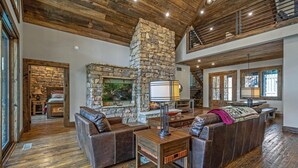 A spacious living room with a stone fireplace, leather sofas, and a wooden ceiling. - Misty Trail Lakehouse - Morganton, GA (Morganton)