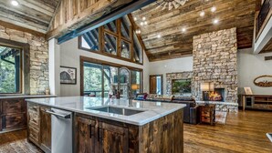 A spacious kitchen with a large island, stone accents, and a stone fireplace. - Misty Trail Lakehouse - Morganton, GA (Morganton)
