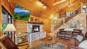 A log cabin interior with a stone fireplace, leather furniture, a wooden staircase, and a scenic mountain view through a window. - Early Rise - Blue Ridge  (Blue Ridge)