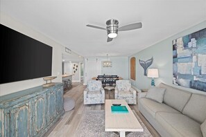 A living room with a ceiling fan, a large painting, and a dining area with two chairs and a table.