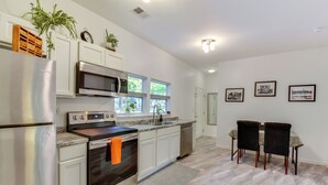 A modern kitchen with stainless steel appliances, white cabinetry, and a dining area with two chairs. - Clemson Game Day Cottage w/ Fire Pit (Central)