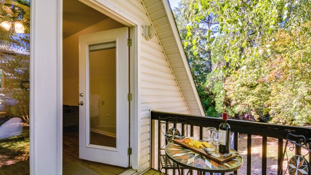 A covered outdoor seating area with a table and chairs, a door leading inside, and a view of trees and a garden. - Clemson Game Day Cottage w/ Fire Pit (Central)