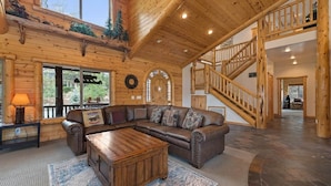 A log cabin interior with a large L-shaped sectional sofa, a wooden coffee table, a fireplace, and a wooden staircase. - The Golden Oak Retreat (Big Bear Lake)