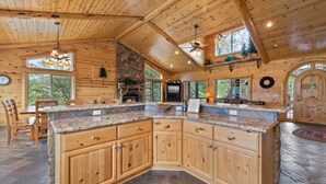 A spacious kitchen with wooden cabinets, a stone countertop, and a fireplace. - The Golden Oak Retreat (Big Bear Lake)
