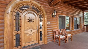 A log cabin with a large wooden door, two windows, and a porch with two wooden chairs. - The Golden Oak Retreat (Big Bear Lake)