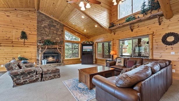 A log cabin interior with a stone fireplace, leather sofa, and a television. - The Golden Oak Retreat (Big Bear Lake)
