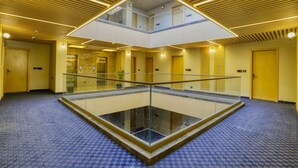 Um átrio amplo em vários níveis, com piso de vidro, teto de madeira e paredes amarelas.