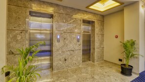 Área de elevador moderna com paredes de mármore e planta em vaso.