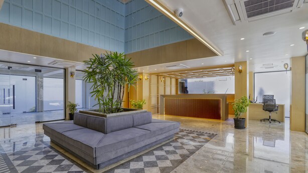 Um hall amplo com piso xadrez, um sofá cinza e plantas em vasos.
