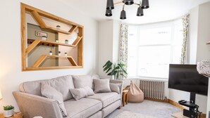 A living room with a sofa, a coffee table, a TV, a bookshelf, and a window with curtains. - Dovestones (Keswick)