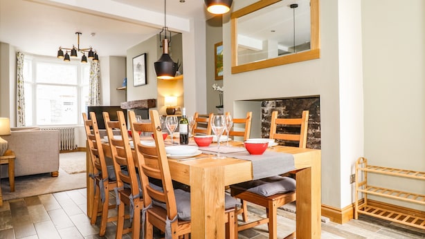 A dining area with a wooden table set for six, surrounded by wooden chairs with cushions. - Dovestones (Keswick)