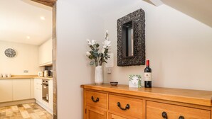 A wooden cabinet with drawers, a vase with flowers, a wine bottle, and a mirror on a wall. - Dovestones (Keswick)