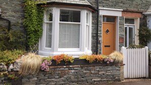 A stone house with a bay window, a wooden door, and a white picket fence. - Dovestones (Keswick)