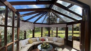 A sunlit room with a glass ceiling, a curved sofa, and a round coffee table. - Hidden gem with hot tub  and tennis court in idyllic East Sussex  countryside . (Hellingly /Hailsham)