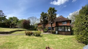 A house with a brick exterior, a lawn, and a dog lying on the grass. - Hidden gem with hot tub  and tennis court in idyllic East Sussex  countryside . (Hellingly /Hailsham)