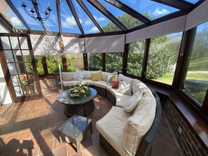 A sunroom with a glass ceiling, a sectional sofa, a round coffee table, and a small side table. - Hidden gem with hot tub  and tennis court in idyllic East Sussex  countryside . (Hellingly /Hailsham)