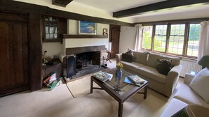 A cozy living room with a fireplace, a sofa, a coffee table, and a window with a view of greenery. - Hidden gem with hot tub  and tennis court in idyllic East Sussex  countryside . (Hellingly /Hailsham)