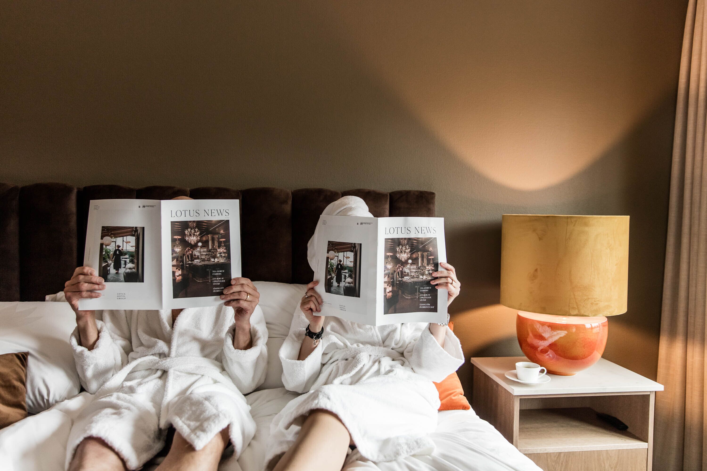 Una habitación de hotel con una cama, una mesita de noche con lámpara y una revista.