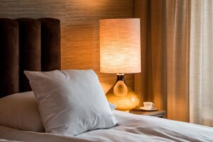 Una cama bien hecha con un almohadón blanco y una lámpara en la mesita de noche.