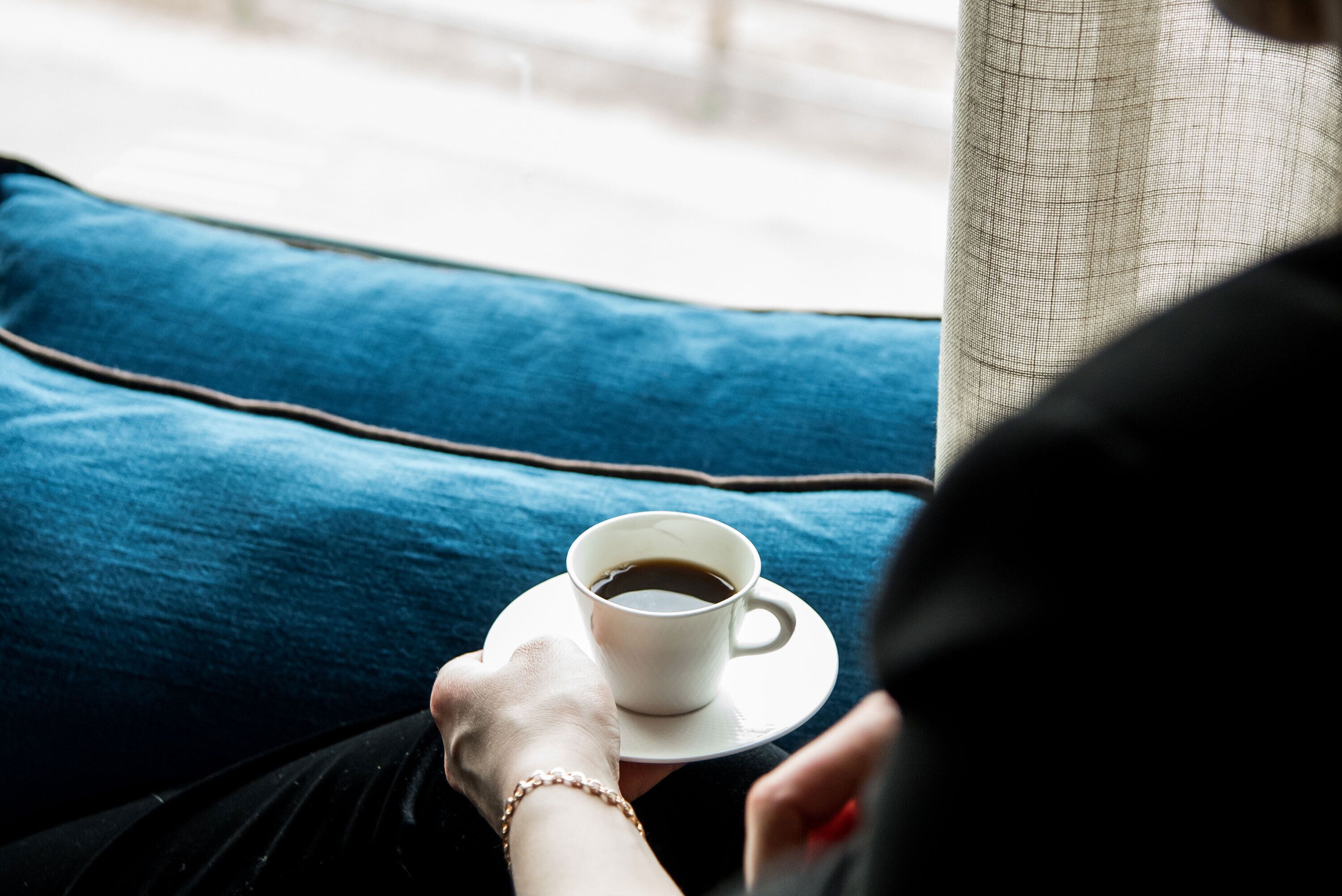 A person holding a cup of coffee on a blue cushioned seat.