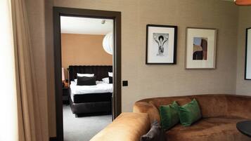 A hotel room with a brown sofa, a bed with white bedding, and two framed pictures on the wall.