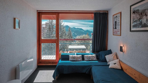 Ein Schlafzimmer mit zwei Betten, einem Balkon mit Bergblick und einem Fenster mit Vorhängen.