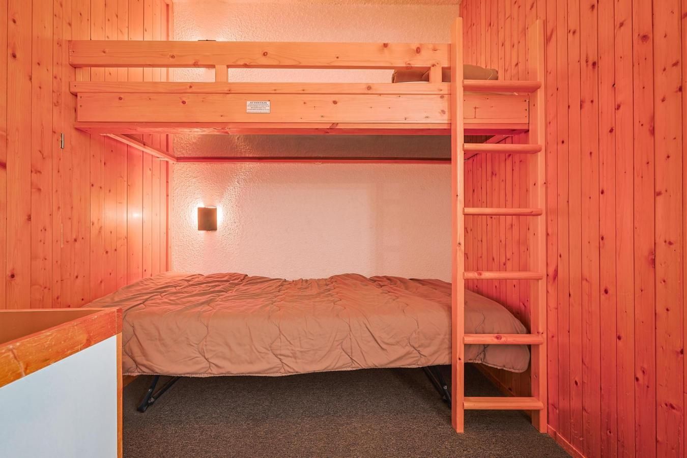 Une chambre avec un lit superposé, une échelle en bois, un lit simple et une petite étagère.