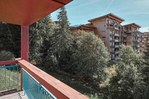 A wooden balcony with a view of a multi-story building surrounded by dense trees. - 6th floor, view resort, balcony, tv, 40m², Les Arcs (Les Arcs)