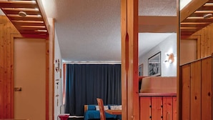 Ein Korridor mit Holzwänden und Teppichboden führt zu einem Zimmer mit Bett, Tisch und Stuhl.