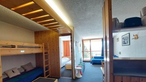 Ein Schlafsaalzimmer mit Etagenbetten, einer kleinen Sitzecke mit Hocker und einem Fenster mit Vorhängen.