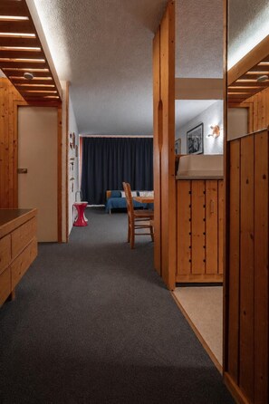 A room with a wooden wardrobe, a bed with a blue cover, a red chair, and a wooden table.
