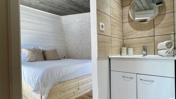 Una camera da letto con un letto di legno, un comodino bianco e un bagno con lavabo e specchio.