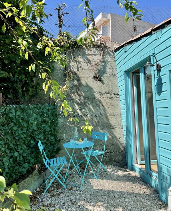 A blue outdoor seating area with a table and chairs, a bottle, and a bowl of fruit. - Adorable detached outbuilding with spa area at extra cost (CAGNES-SUR-MER)