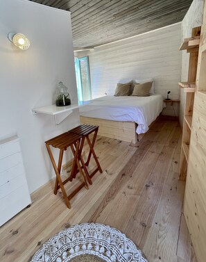 A cozy bedroom with a wooden floor, a bed with white bedding, a small wooden table, and a shelf with a glass jar. - Adorable detached outbuilding with spa area at extra cost (CAGNES-SUR-MER)