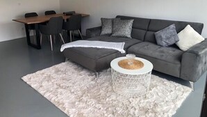 Un salon moderne avec un canapé gris, une petite table d’appoint ronde blanche et un tapis à poils longs blanc.