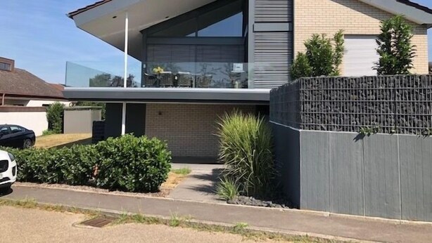 Une maison moderne à deux étages, dotée d’un toit plat, de grandes fenêtres et d’un balcon.