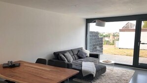 Un espace de vie moderne comprenant une table à manger en bois, un canapé gris et une grande porte-fenêtre coulissante donnant sur un espace extérieur.
