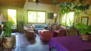 A cozy living room with a sofa, armchairs, and a table. There are several potted plants and a television on the wall. - Charming house between sea and countryside (Binic-Étables-sur-Mer)