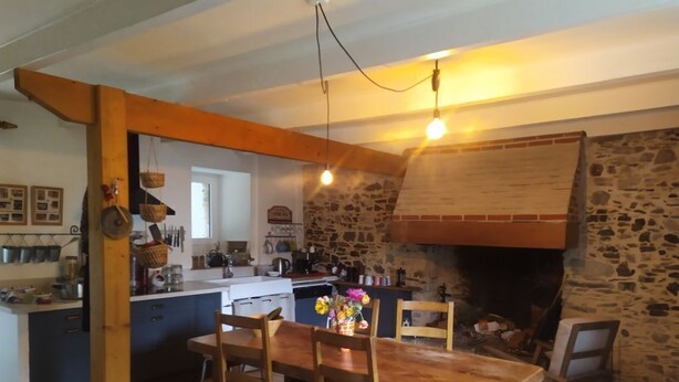 A rustic kitchen with a stone wall, wooden beams, and a hanging light fixture. - Charming house between sea and countryside (Binic-Étables-sur-Mer)