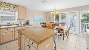 A kitchen with a granite island, wooden cabinets, a dining area with a table and chairs, and a view of the outside through large windows. - Beaches and Dreams by Book That Condo (Panama City Beach)