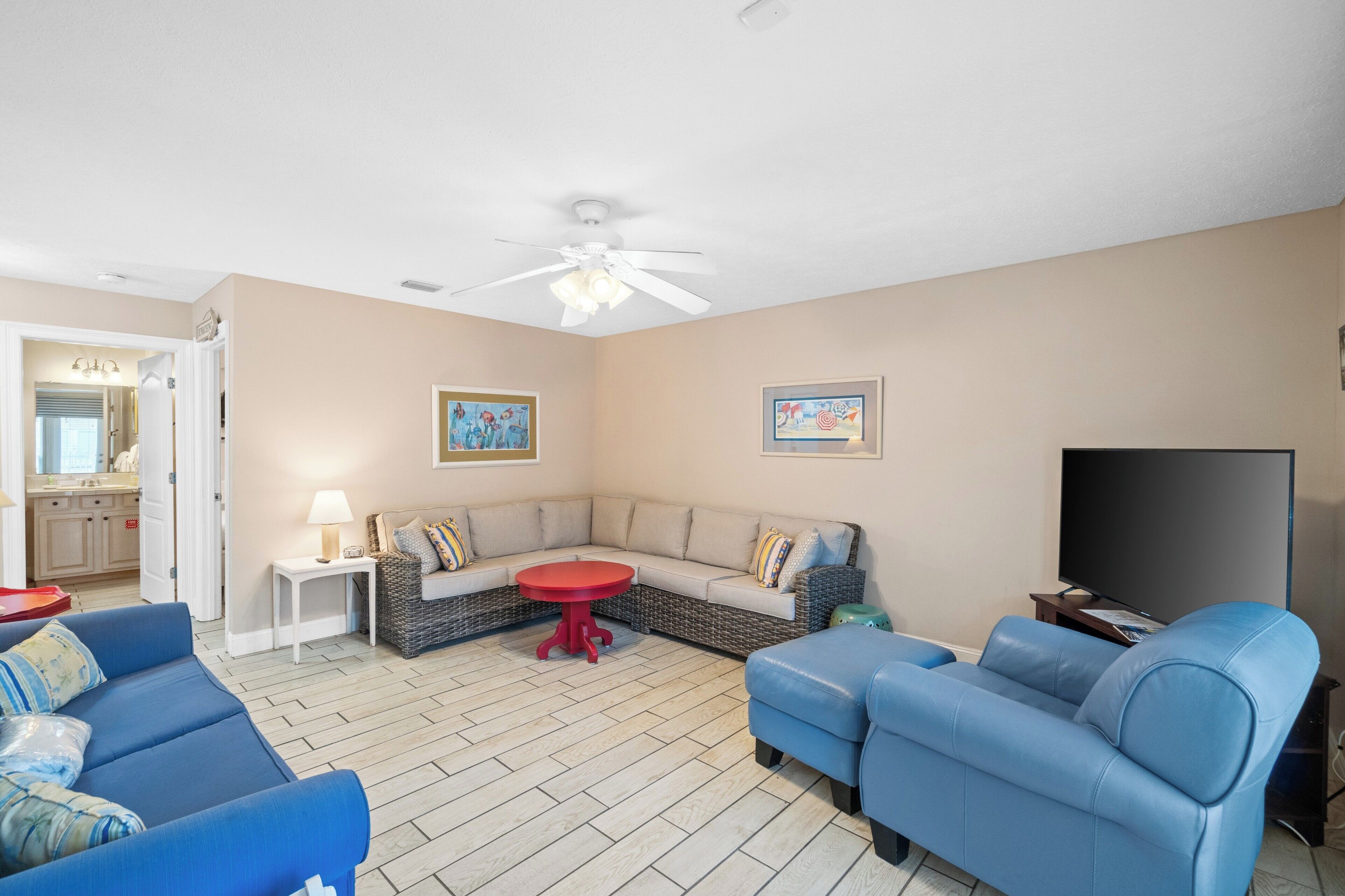 A living room with a sectional sofa, a blue armchair, a red table, and a ceiling fan.