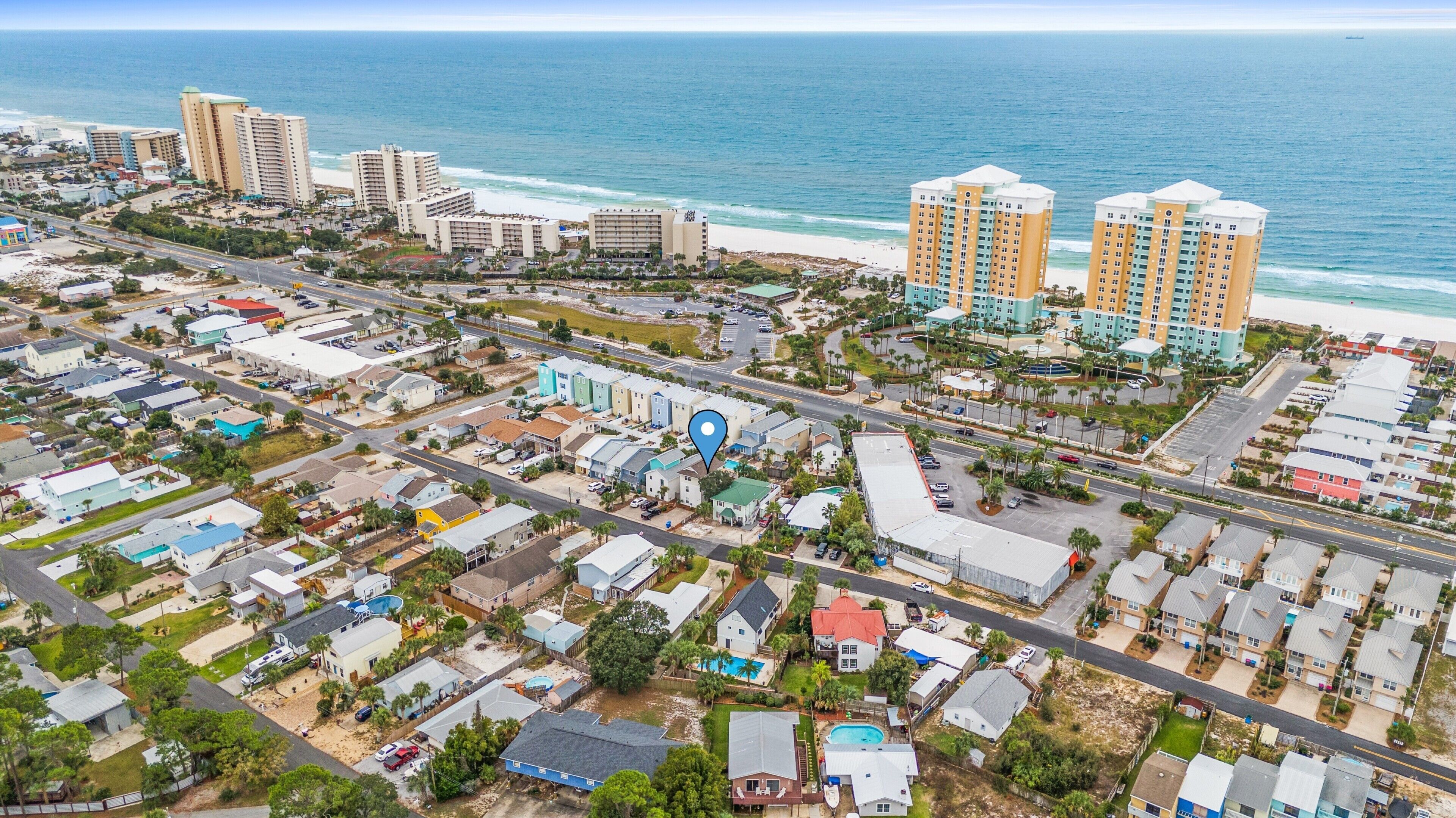 An aerial view of a coastal residential area with beachfront hotels, roads, and houses.