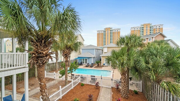 A residential area with a swimming pool, palm trees, and a white fence. - Beaches and Dreams by Book That Condo (Panama City Beach)