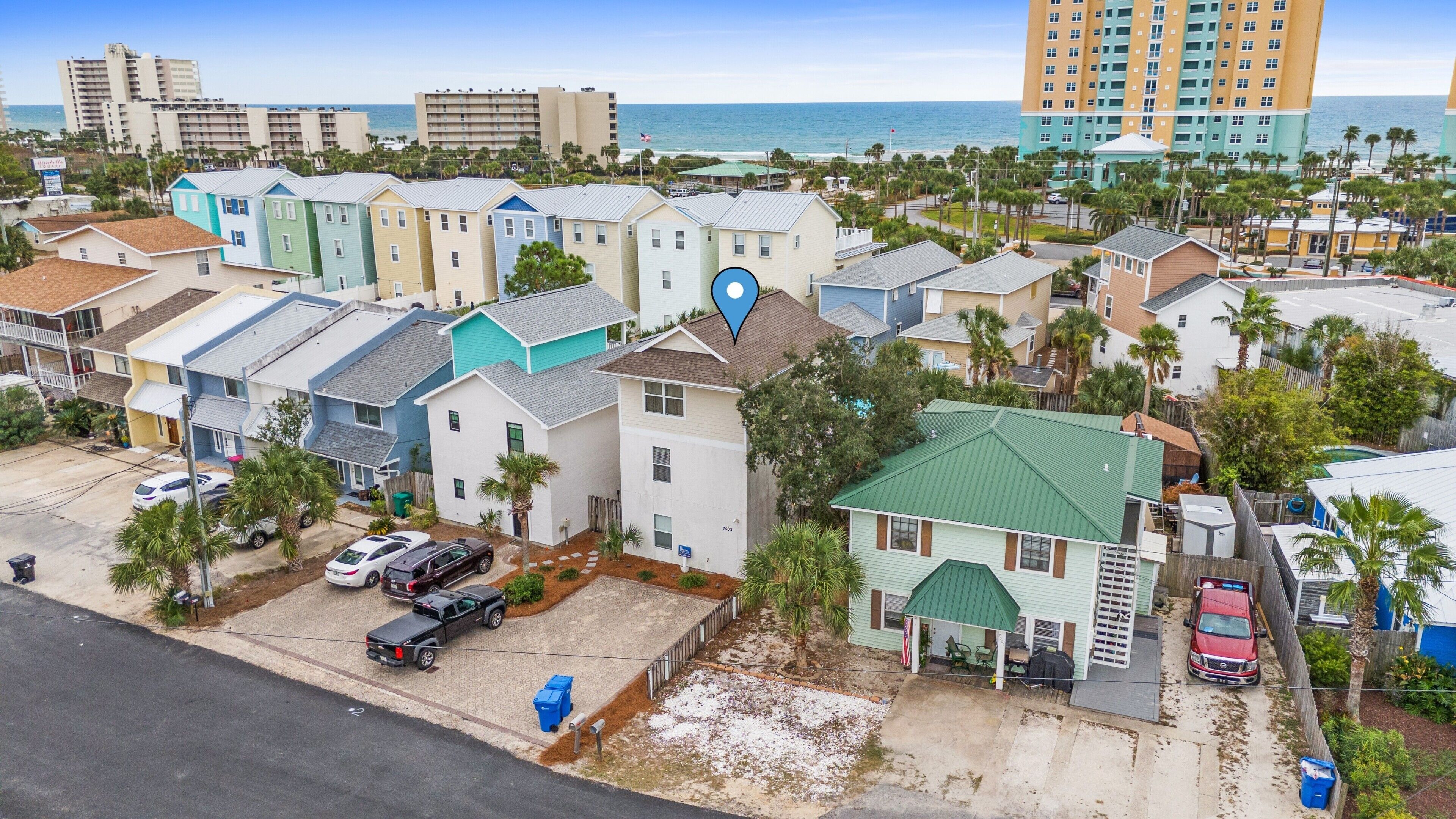 A coastal residential area with colorful houses, a parking lot, and a view of the beach and ocean.