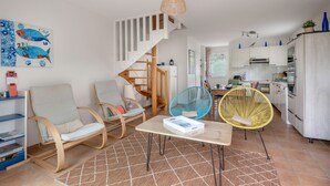 En moderne stue med trappe, træstole, et bord med en bog og et køkken i baggrunden.